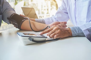 An close-up view showing a doctor's hands working to measure a young adult male's blood pressure with a digital sphygmomanometer a.k.a. blood pressure monitor.