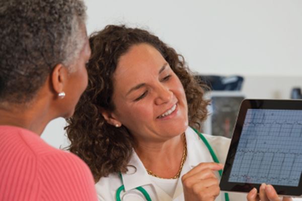 A female doctor and a female patient looking at a heart rhythm on an iPad.