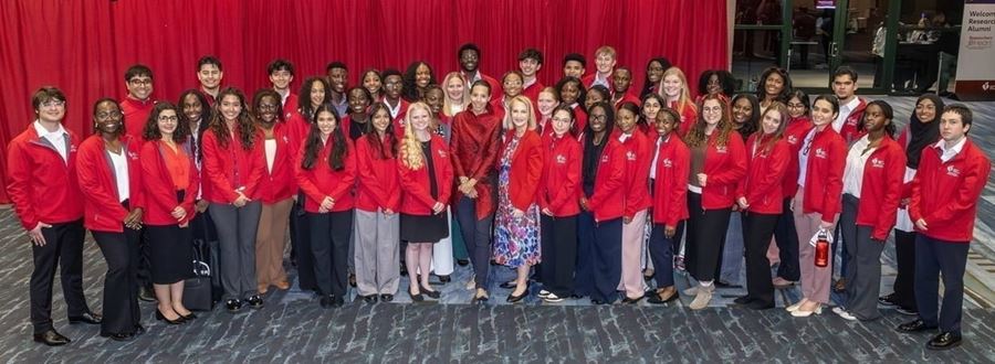 Large group of scholars standing in front of a red drape