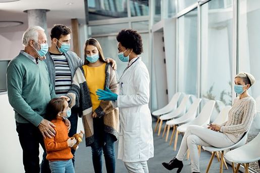 Extended family and their doctor wearing protective face masks while communicating in a hallway at medical clinic.