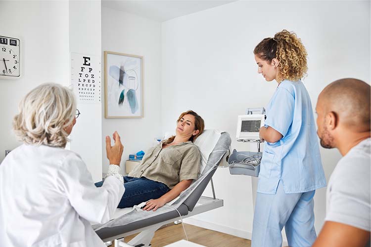Doctor talking to patient in doctors office with family member and nurse in room