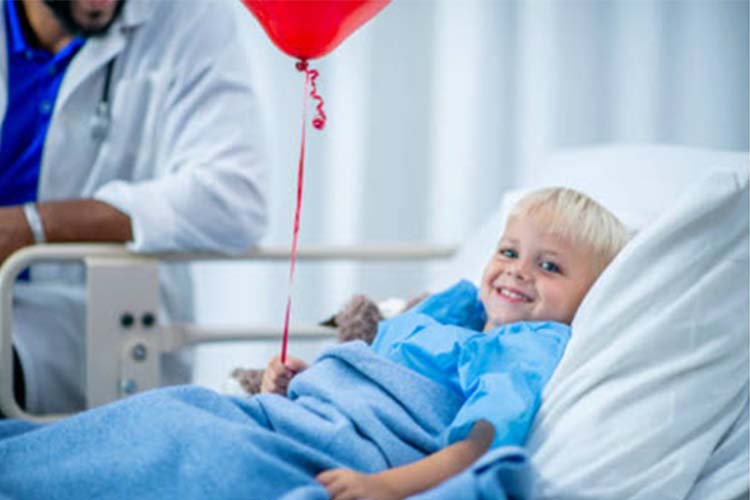 Little boy smiling in hospital bed with a balloon