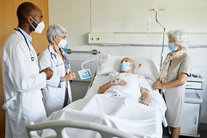 Two doctors, wearing protective face masks, talking to senior patient and his wife in ICU.