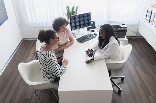 Female doctor telling mother and daughter medical results at doctor’s office using digital tablet