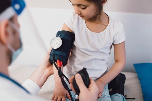Male pediatrician measuring blood pressure of girl in medical clinic during COVID-19