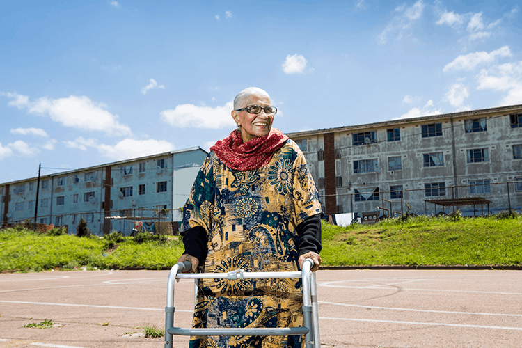 Elderly woman with walker in front of dilapidated housing building