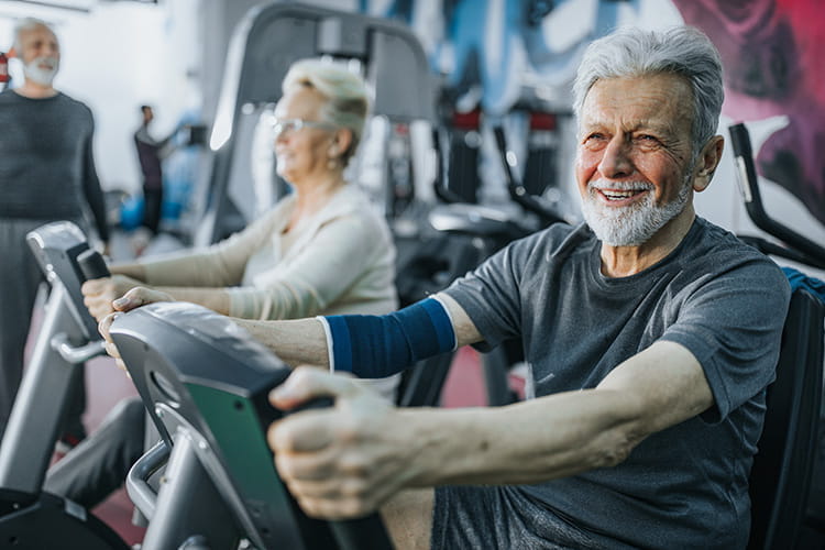 Senior male smiling exercising on stationary bike in a gym