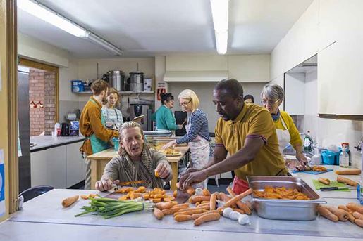 Volunteers working in a soup kitchen/food bank laughing together, preparing food.