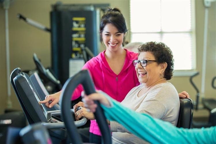 Woman on rehabilitation bike with therapist by her side